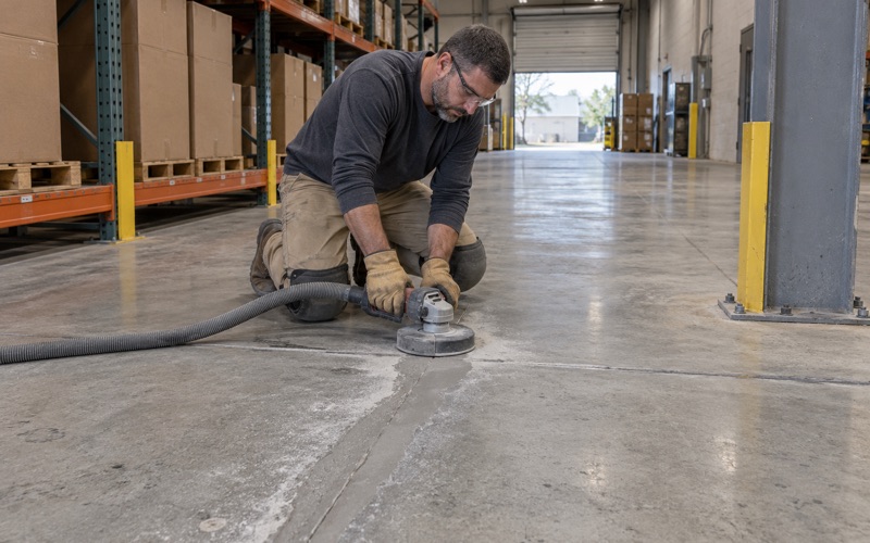 A spalled control joint in a Hoffman Estates warehouse aisle rebuilt with filler and ground flush before recoating.