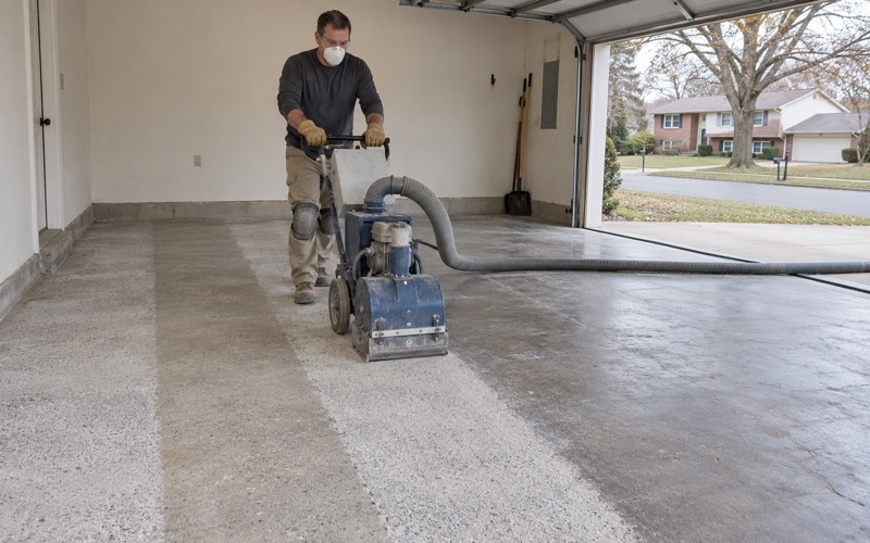 A walk-behind shot blaster opening up a Hoffman Estates garage slab, the cleaned lane pale beside the old sealed concrete.